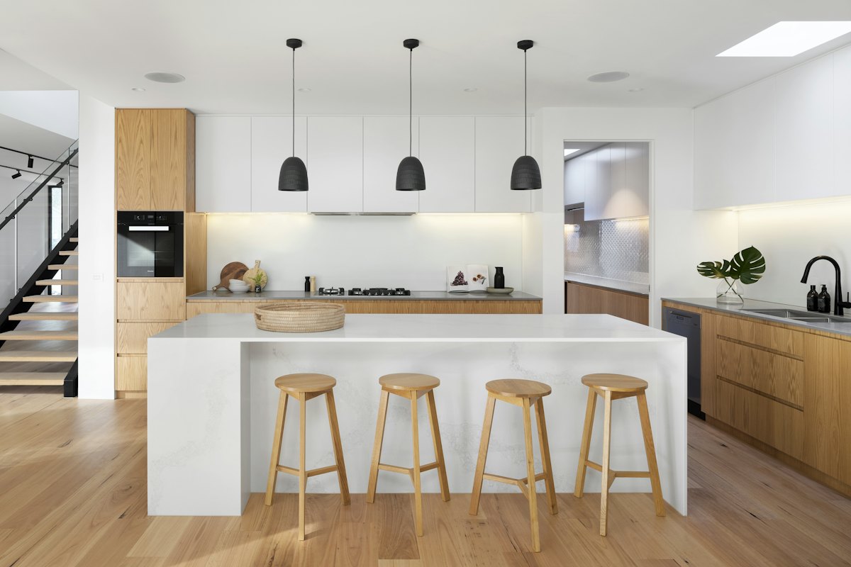 Open kitchen with a white island, wood stools and pendant lights