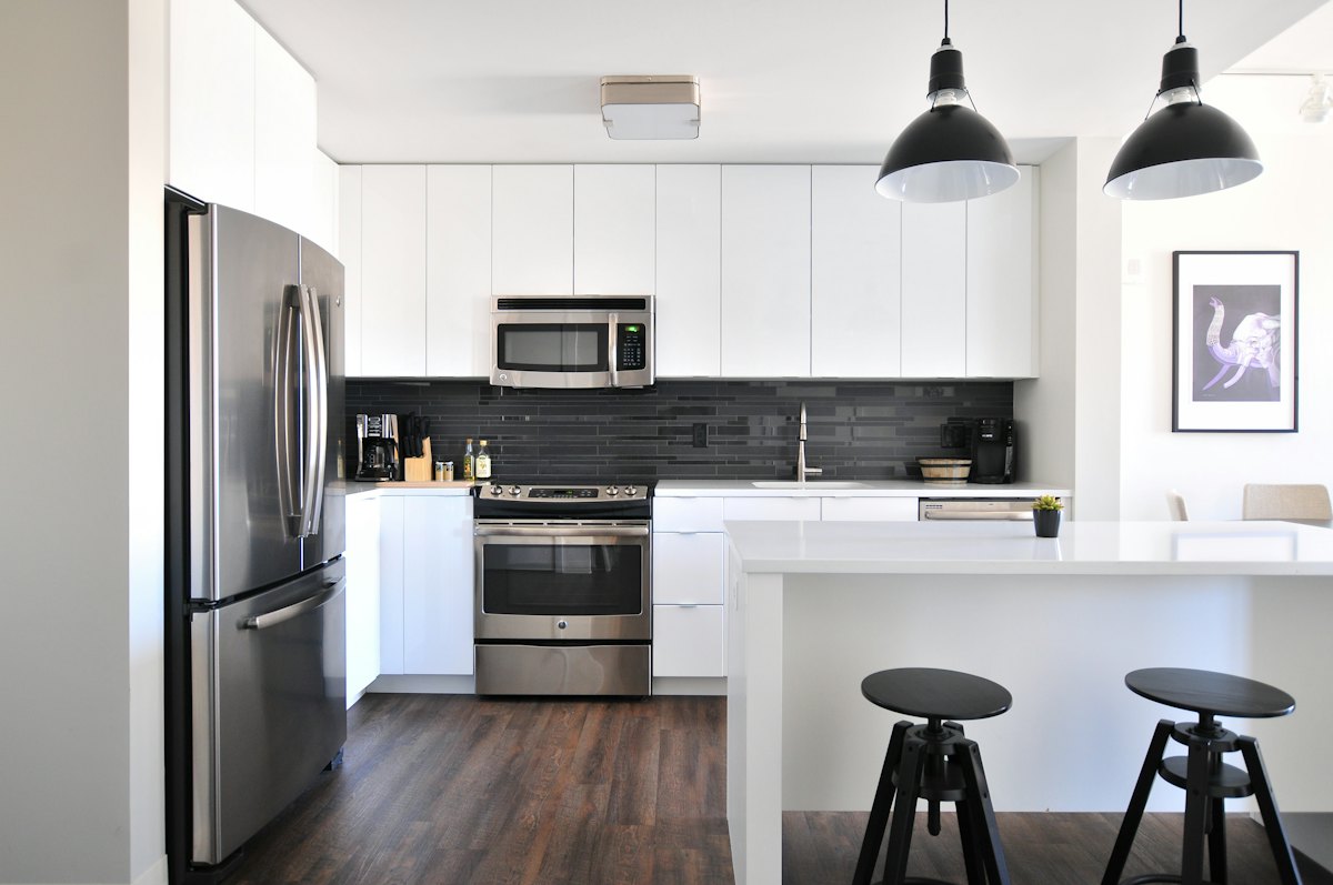 White kitchen with stainless appliances, dark backsplash and pendant lights over the island