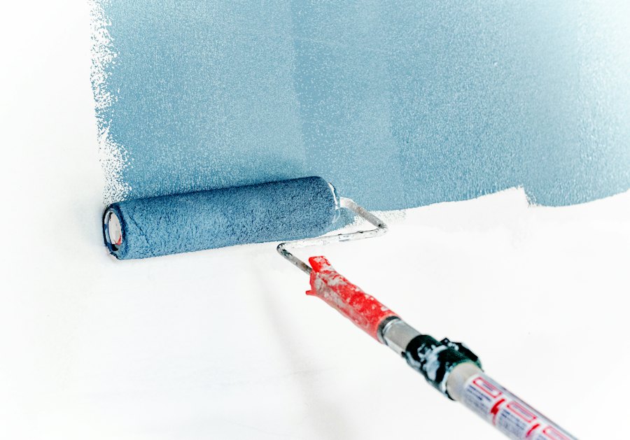 Paint roller applying blue paint to a white wall