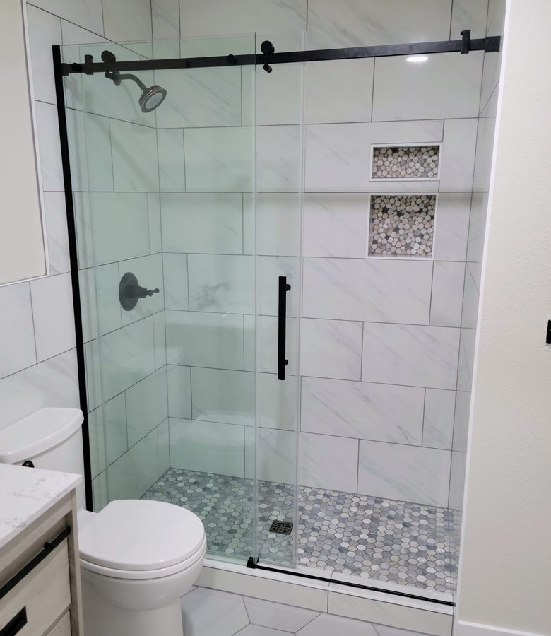 Walk-in shower with frameless glass and pebble floor by RLC Construction
